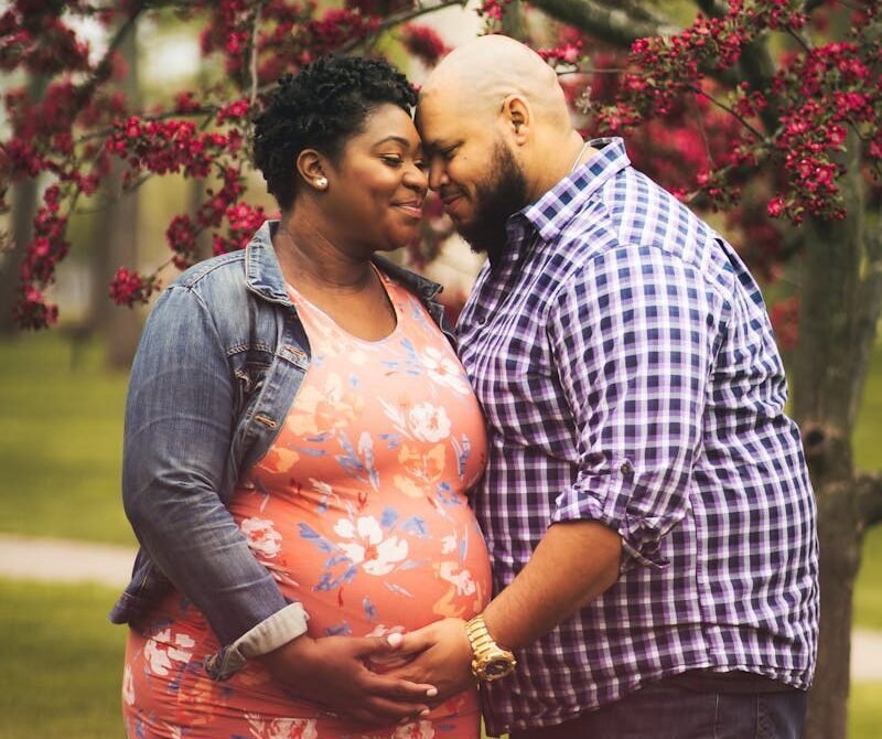 Pregnant black woman caressing husband near tree